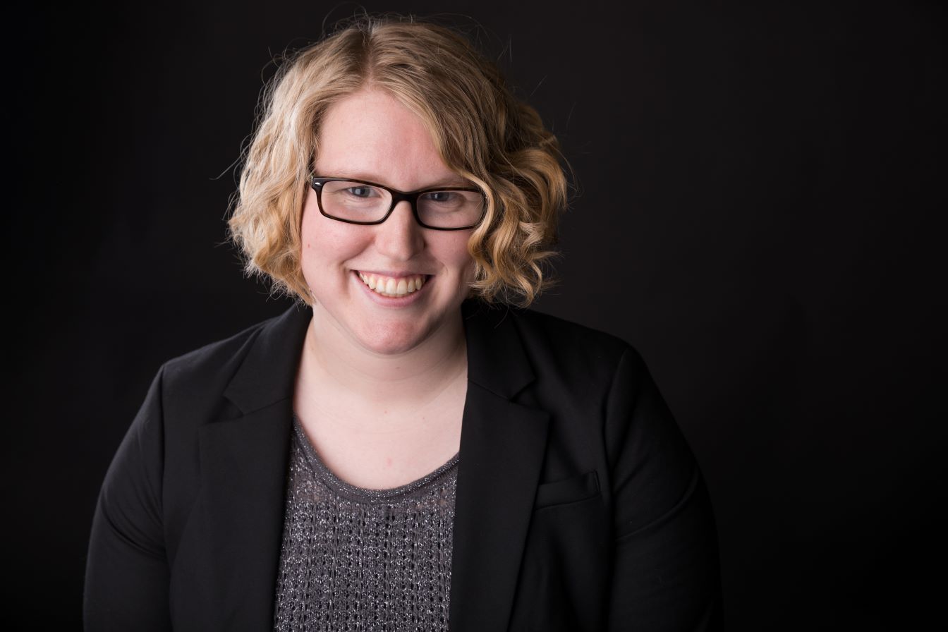 Allison McIntosh poses, smiling, in front of a black background