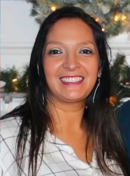 A picture of a smiling person with blue eyeshadow and long brown hair. They are looking into the camera.