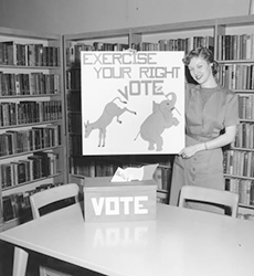 Voting display Black and white photo of a woman with voting display at the Temporary Library Headquarters, Merriam. 1956.