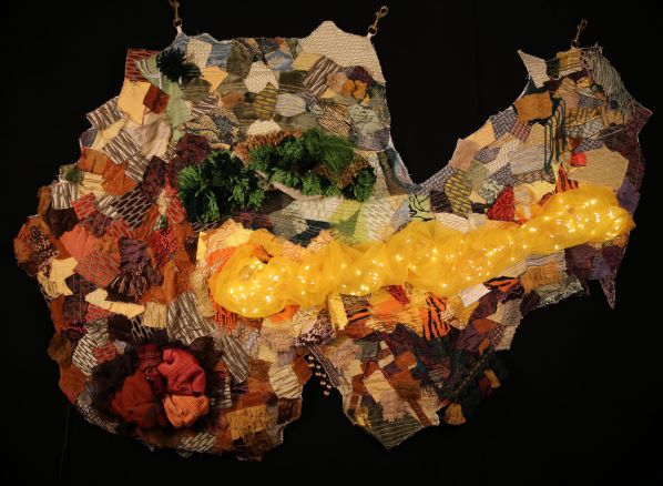 Mixed media textile hanging collage made up of fabrics in earth tones, other textural attachments and lights.