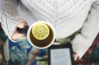 A person holding a cup of tea with lemon and an eReader