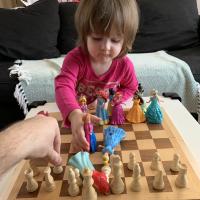 A man plays chess with a toddler who is using dolls in place of chess pieces