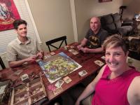 Three people sit at a table playing a board game