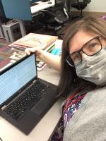 A woman in glasses and a face mask reads text on a computer