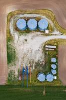 Aerial view of rural lot with sparse grass and multiple blue silos (3 large, 2 medium and 3 small).