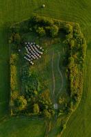 Aerial view of treed, grassy field scattered with hay bales.