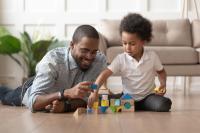 An adult and child play with wooden blocks, sitting on the floor