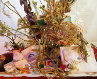 Photograph of still life arranged with dried flowers, white t-shirt, dollar bill and paper packaging.