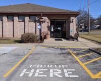 A parking spot with "Pick Up Here" spraypainted on the cement, in front of a Library