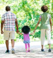 Two adults and a child walk hand in hand down a park path
