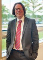 Sean Casserley poses in front of a window in a suit with a red tie, hands in his pockets