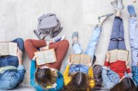 a row of young people viewed from above, sitting against a wall and reading books