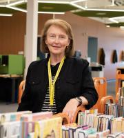 a woman wearing a yellow volunteer lanyard poses behind carts full of books