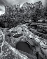 Black and white photograph of rock formations in the background and natural small pools in the foreground.