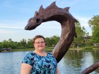 bethany griffith poses in front of a dragon statue in a park