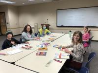 young people attend a Scribbler Society program, gathered around a table with writing and other creative materials in front of them