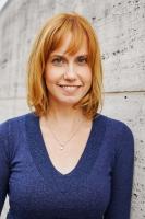 A person shown from waist up in a blue shirt with reddish blonde hair smiling at the camera