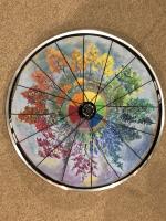 Painting of multicolored trees set behind bicycle wheel spokes.