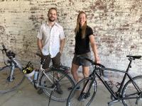 nick ward-bopp and laura fox pose in front of a painted brick wall with two bikes