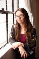 A person with long brown hair and glasses leaning one elbow on a widow sill