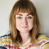 A person with brown hair and bangs and a yellow striped shirt looks into the camera