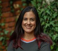 A person with long dark hair standing on front of a brick wall