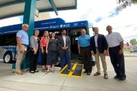 a group of people in business attire standing in front of a blue bus with the wheelchair ramp deployed