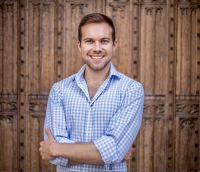 A person in a blue shirt in front of a wooden wall smiles at the camera