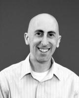 A black and white photo of a bald person in a button down shirt smiling at the camera