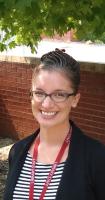 A person with glasses and a black and white striped shirt and red lanyard smiles at the camera