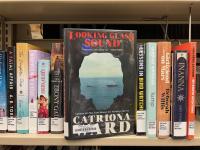 The book The Looking Glass Sound by Catriona Ward being pulled off of a bookshelf full of other books