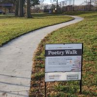 A sign saying "poetry walk" with a park walking trail behind it