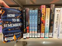 The book How to Be Remembered by Michael Thompson being pulled off of a library bookshelf full of other books