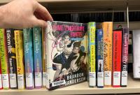 The book Yumi and the Nightmare Painter on a shelf with other Library books