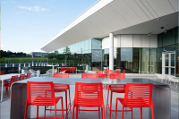 Photo depicting the outdoor patio at Monticello. Orange metal chairs and tables. The building is to the right and trees and skyline in the distance.