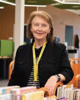 Photograph of a female volunteer with arm resting on cart of books.