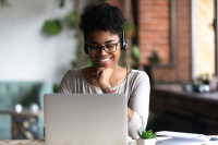 A young smiling African American woman sits behind a laptop.