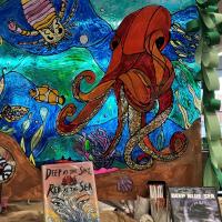 An octopus painted as a the backdrop for a library display of books and dvds about the ocean