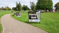 Photo of a sign that reads Poetry Walk in a scenic park with a winding path.