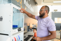 Photo of a man opening the door to a 3D printer.