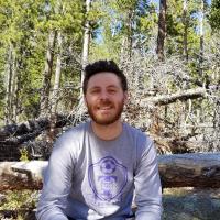 Dan Wikiera Dark haired man with a beard and mustache in a grey Truman Bulldogs longsleeved shirt in the woods
