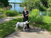 Blond woman in black clothes with a white spotted dog standing in front of a lake