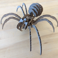 Table with wooden tabletop. On the table, an unpainted laser cut cardboard spider, assembled.