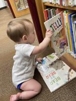 a kneeling baby pulls a picture book off of a low library shelf