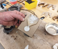 A hand holding a mold with casted metal inside.