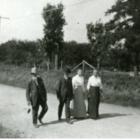 A black and white photo of four people, two in skirts and two in suits, walking down a road together