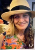 woman smiling with long hair braided on one side wearing a hat with a black band