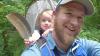 Ian James Jannin-Hughes blonde bearded man in ball cap and blue shirt with baby in a backpack holding a feather