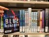The book The Blue Monsoon on a shelf with other Library books